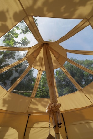 Een tent met een geometrisch ontwerp en meerdere ramen, die uitzicht biedt op de omliggende begroeiing.