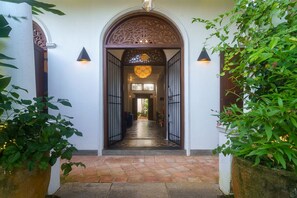 Un couloir orné d’une arche décorative, doté d’un sol carrelé et bordé de part et d’autre de plantes en pot.