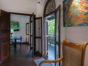 An open wooden door leading to a balcony with a view of greenery.