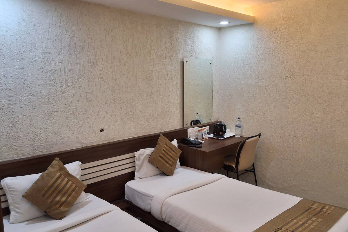 Une chambre d’hôtel avec deux lits, un bureau, une chaise, une machine à café, une bouteille d’eau et un miroir au mur.