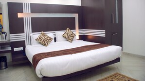 A modern hotel room with a large bed, dark wooden wardrobe, and a built-in shelf with a lamp. - HOTEL ACCORD (Ranchi)