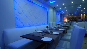 A restaurant with a modern design, featuring a long dining table with white chairs, blue ambient lighting, and a patterned wall. - HOTEL ACCORD (Ranchi)