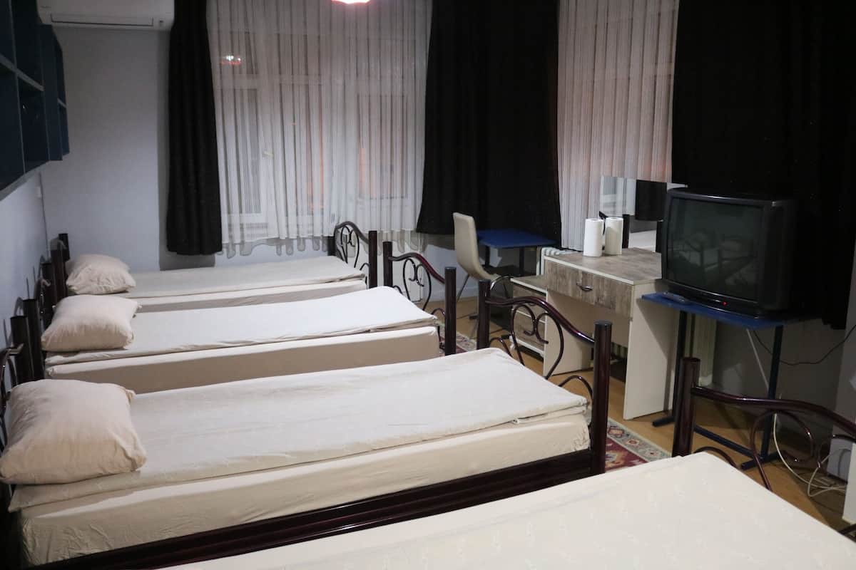 Une chambre avec quatre lits simples, un bureau avec un ordinateur, une télévision et une chaise.