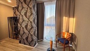 Una habitación moderna con una mesa de vidrio, una silla de madera, una cortina estampada y vistas al exterior.
