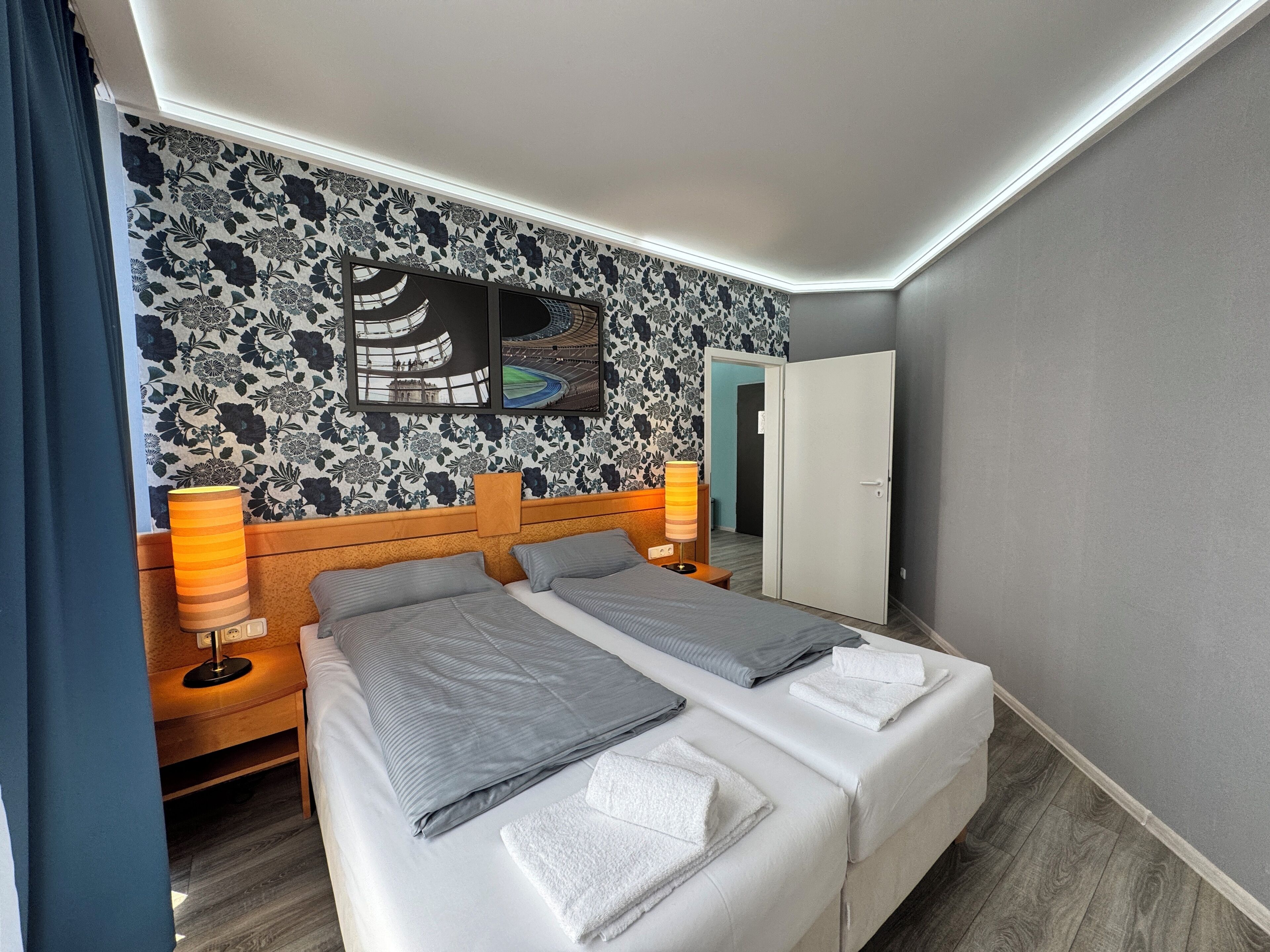 Hotelkamer met een bed, twee nachtkastjes, een lamp, een spiegel en een wand met bloemenpatroon.