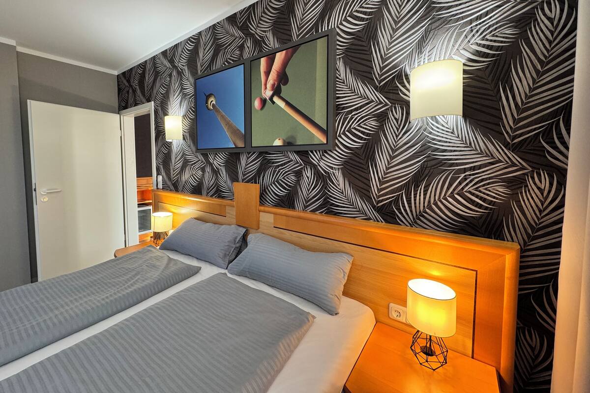 A hotel room with a bed, two wall-mounted lamps, a television, and a patterned wallpaper.