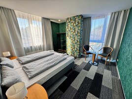 Habitación de hotel con cama, una silla, una mesita y vistas al exterior.