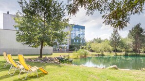Un área verde con sillas reclinables amarillas, un estanque y un edificio moderno al fondo.