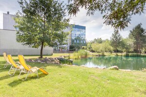 Un área verde con sillas reclinables amarillas, un estanque y un edificio moderno al fondo.