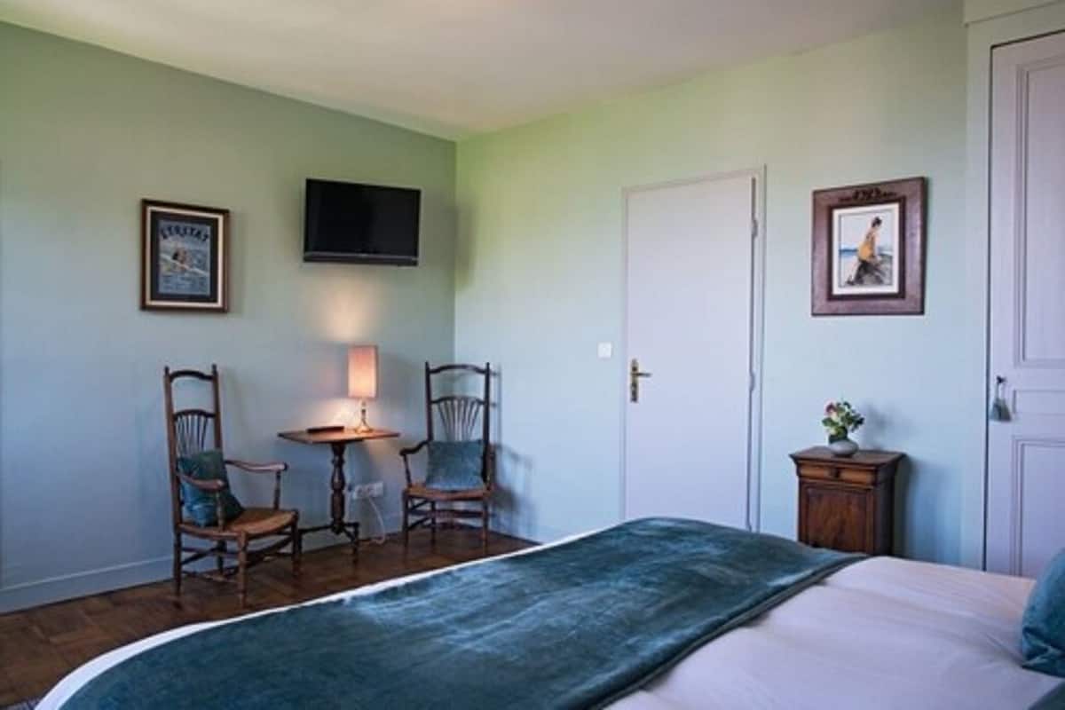 Un dormitorio con una cama, dos sillas, una mesita, un televisor y una puerta.
