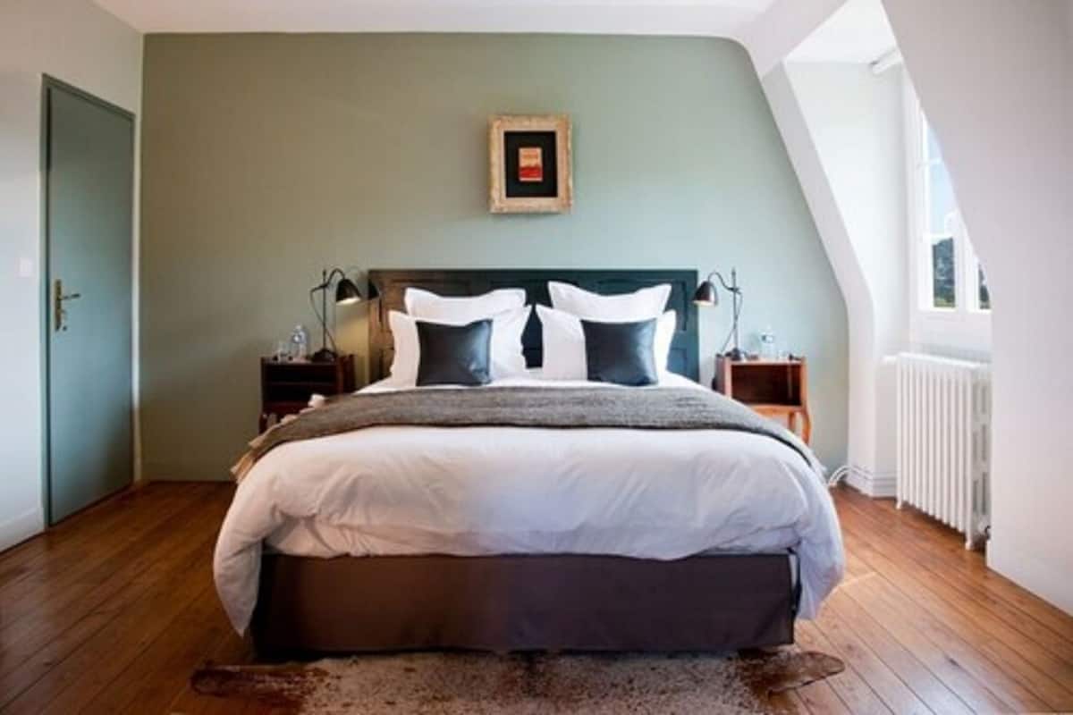 Un dormitorio con una cama grande, un cabecero, dos mesitas de noche, un cuadro enmarcado en la pared y una ventana con vistas.