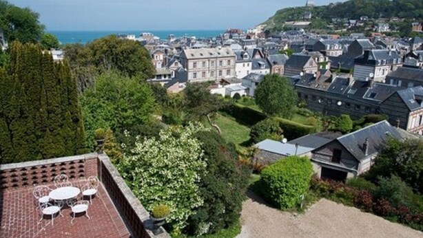 A high vantage point view of a coastal town with historic buildings, a patio with outdoor seating, and a view of the sea. - Castel de la Terrasse (Etretat)