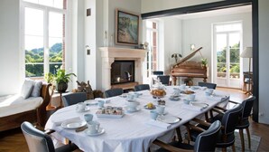 A dining room with a large table set for a meal, a fireplace, and a grand piano. - Castel de la Terrasse (Etretat)