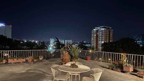 A rooftop terrace with outdoor furniture, potted plants, and a view of city buildings at night. - Apartamentos Reforma (Guatemala City)