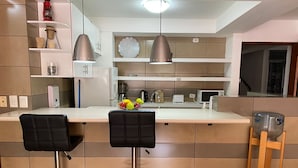 A modern kitchen with two bar stools, a microwave, a kettle, and a water dispenser. - Apartamentos Reforma (Guatemala City)