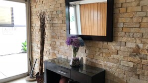 A modern interior with a stone wall, a black console table with a vase of flowers, and a mirror. - Apartamentos Reforma (Guatemala City)