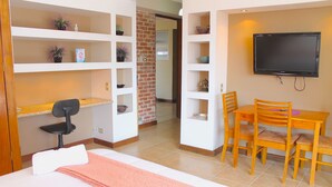 A hotel room with a bed, a desk, a chair, a TV, and shelves with plants and decorative items. - Apartamentos Reforma (Guatemala City)