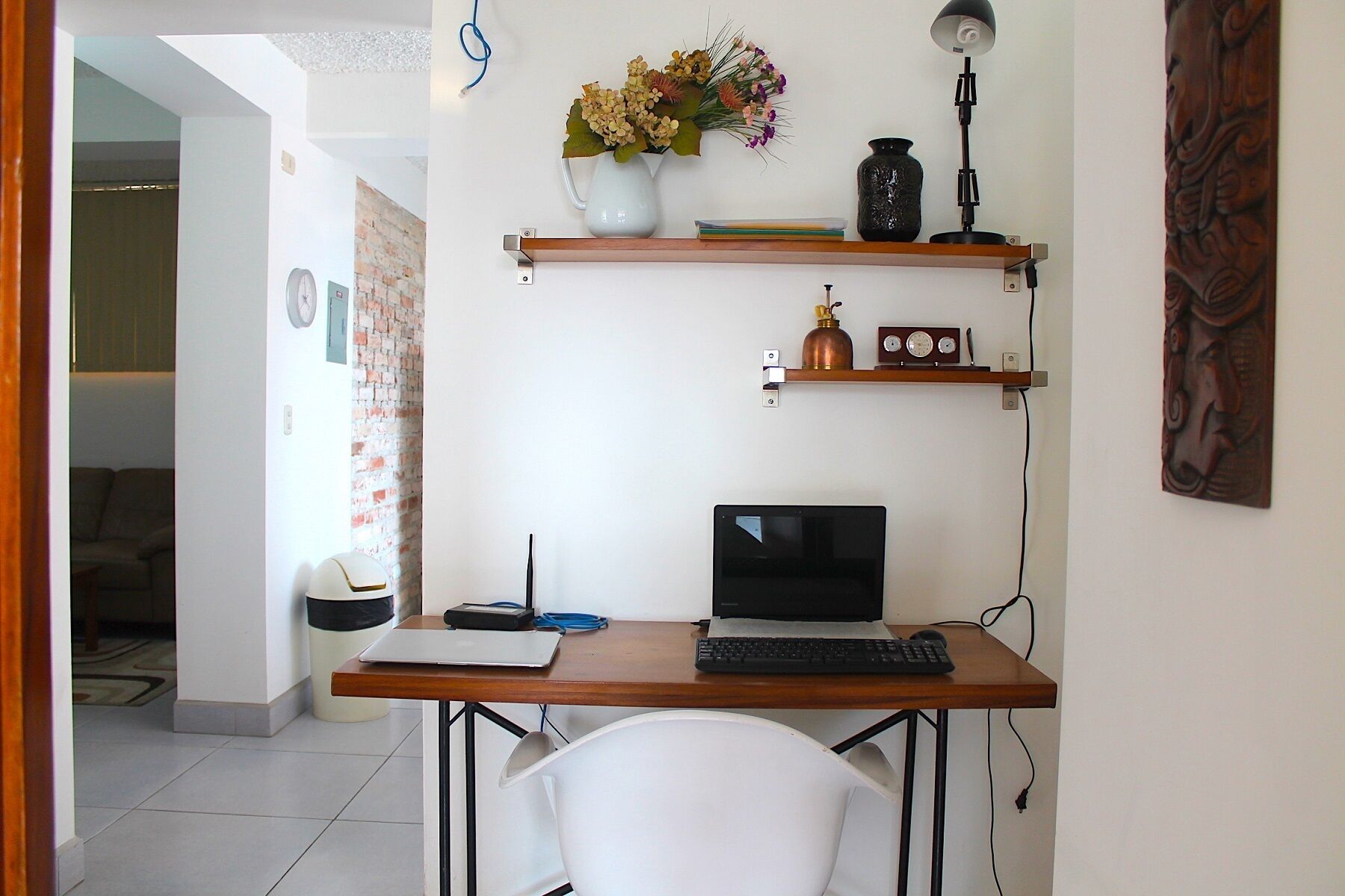 A home office with a desk, computer, and shelves with decorative items.