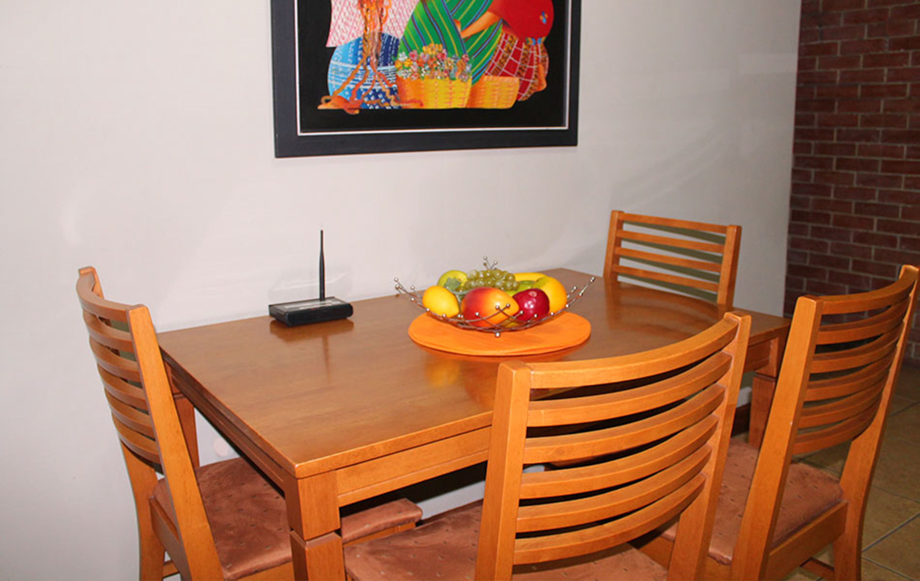 Una mesa de comedor con frutero, sillas y un control remoto.