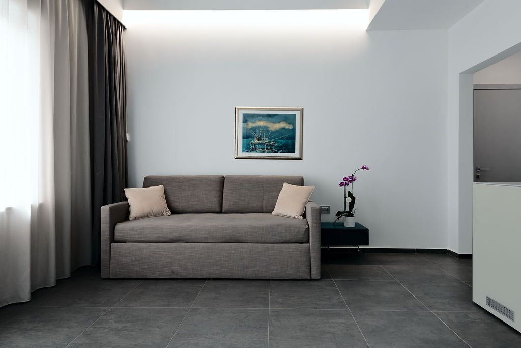Ein modernes Wohnzimmer mit einem grauen Sofa, einem gerahmten Bild an der Wand und einem kleinen Tisch mit einer Blumenvase.