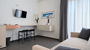 A modern hotel room with a sofa, a TV mounted on the wall, a small desk with two chairs, and a window with curtains. - Nautilus B&B Suite Design (Follonica)