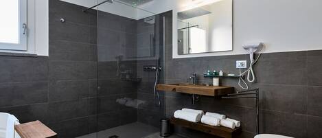 Un baño moderno con ducha de vidrio, tocador de madera, inodoro y un espejo grande.