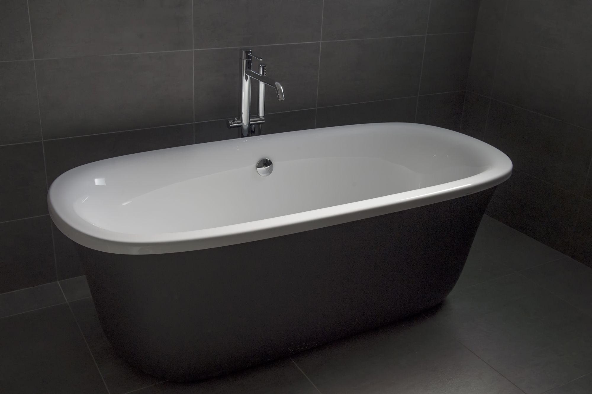 Eine moderne, dunkel gestaltete freistehende Badewanne in einem Badezimmer mit dunklen Fliesen.
