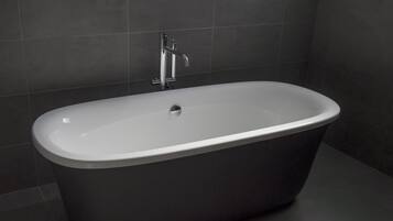 Eine moderne, dunkel gestaltete freistehende Badewanne in einem Badezimmer mit dunklen Fliesen.