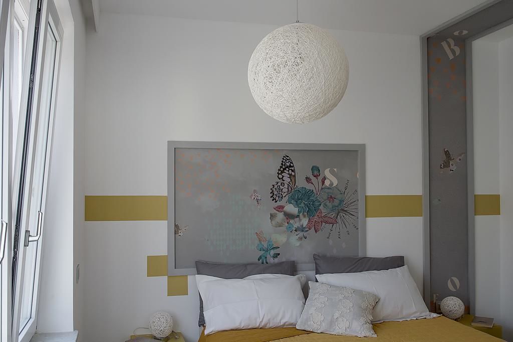 Et soveværelse med en seng, to puder, et billede på væggen, en hængende lampe og en dør med en sommerfugl-udsmykning.