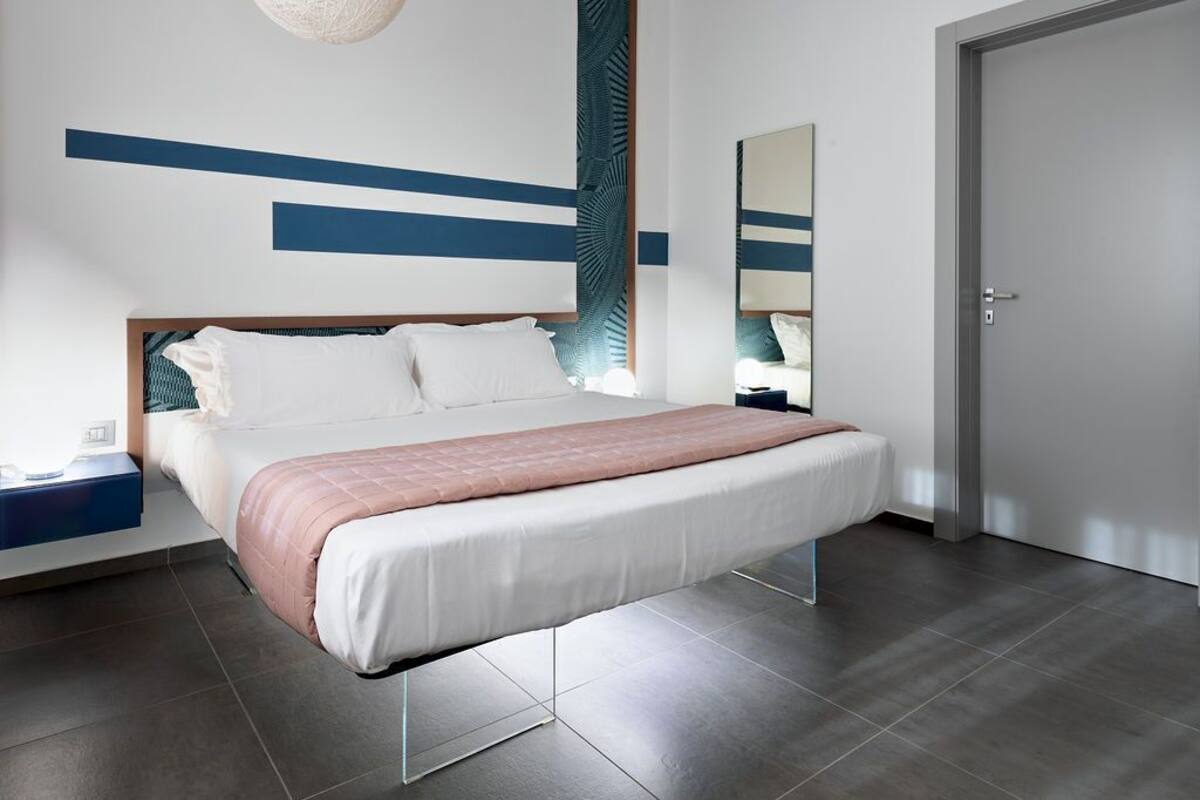 A modern bedroom with a large bed, a bedside table, a mirror, and a door.