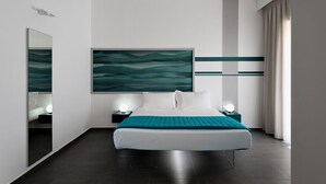 A modern hotel room with a large bed, two bedside tables with lamps, a large abstract painting on the wall, and a view of the city through the window. - Nautilus B&B Suite Design (Follonica)