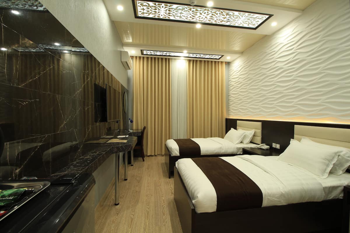A hotel room with two beds, a vanity with a mirror, a desk, and a modern ceiling design.
