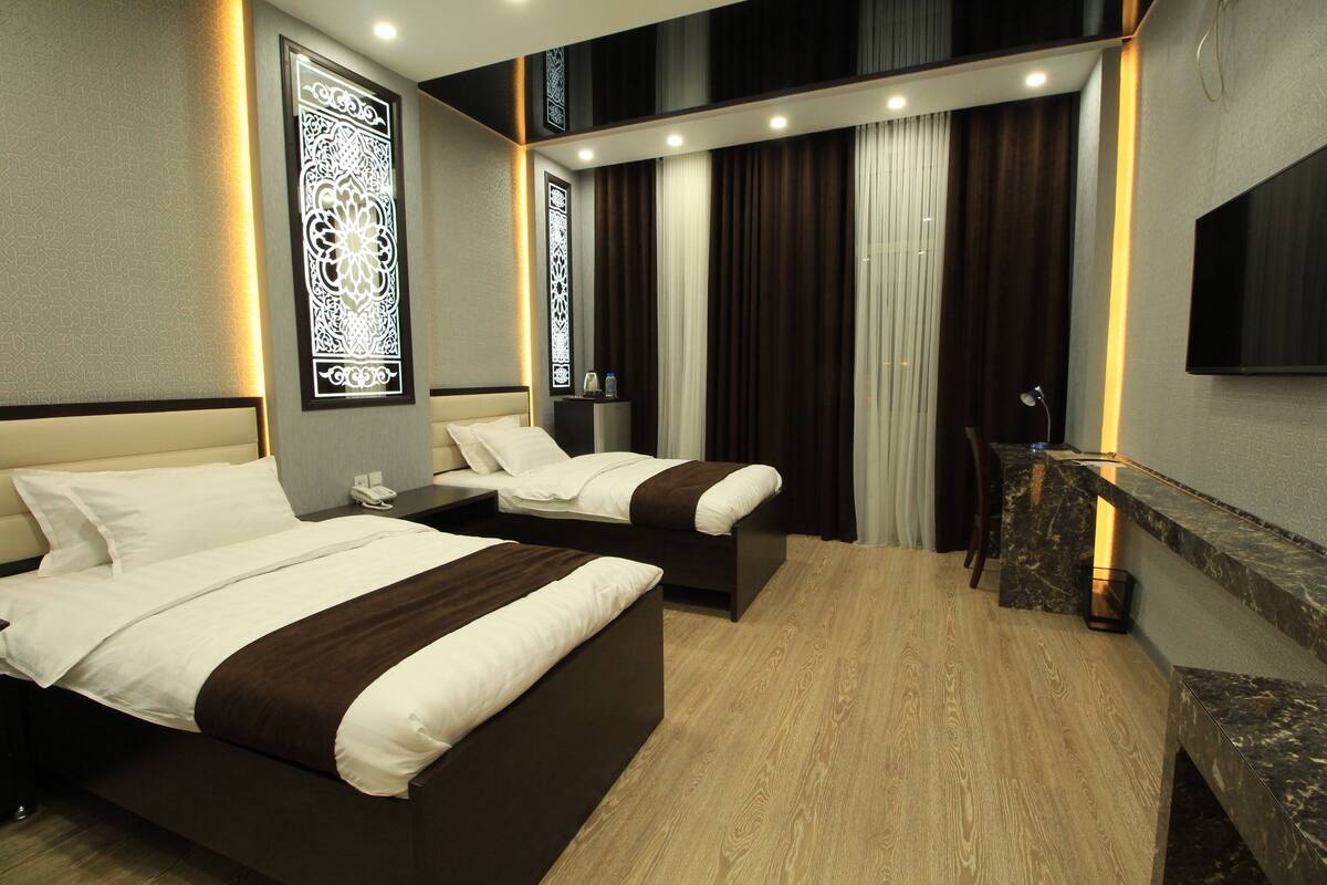A hotel room with two beds, a desk, a chair, a TV, and decorative wall panels.