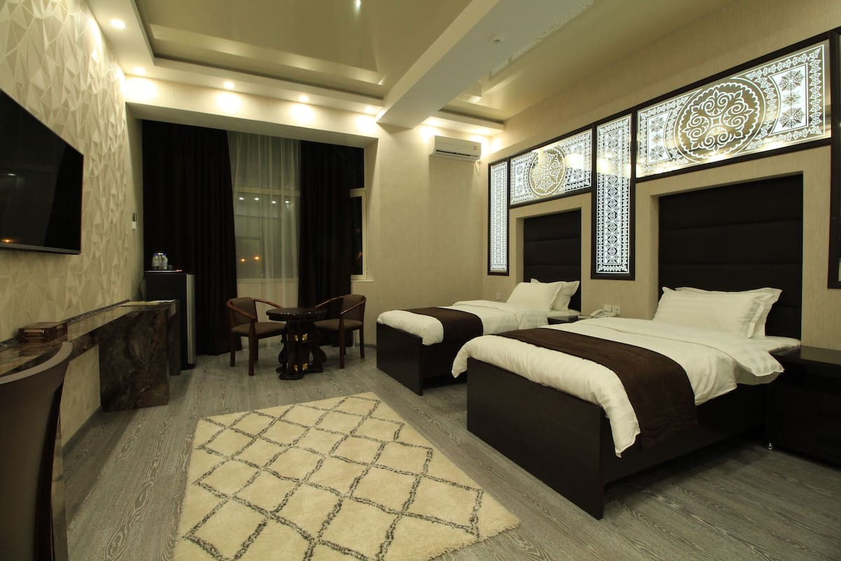 A hotel room with two beds, a desk, a chair, a TV, and decorative wall panels.