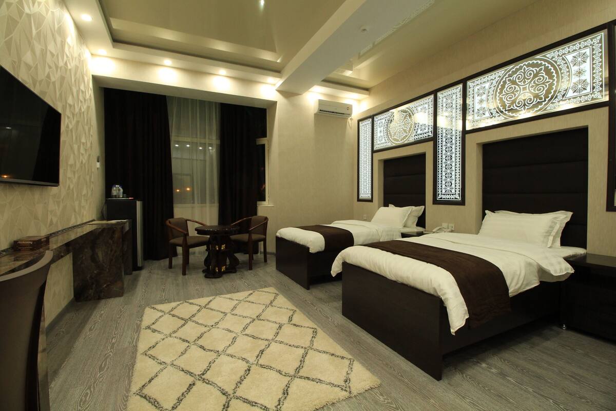 A hotel room with two beds, a desk, a chair, a TV, and decorative wall panels.