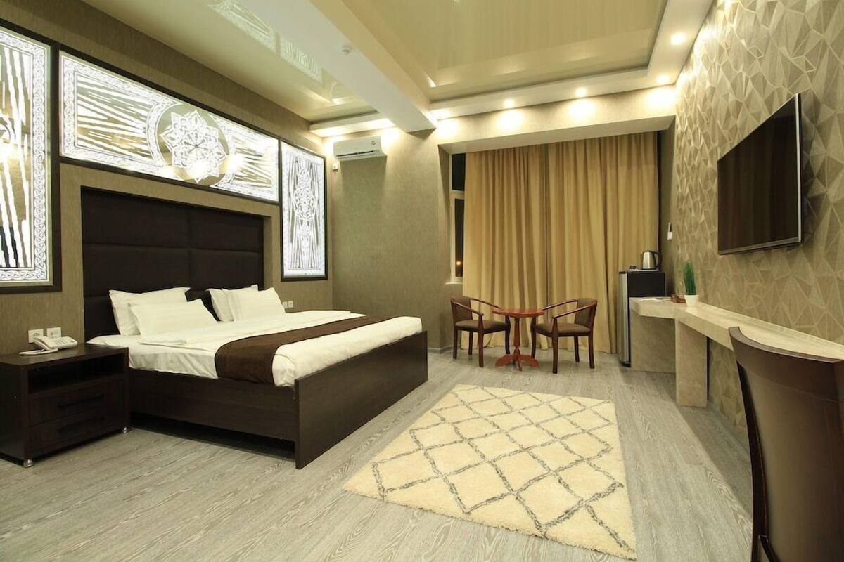 A hotel room with a bed, bedside table, lamp, TV, and a small table with chairs.