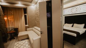 A hotel room with a sofa, a bed, and a partially open door leading to another room.