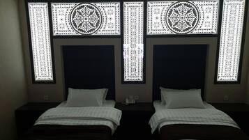 A hotel room with two beds, each with a dark headboard and white bedding. There are decorative window patterns above the beds.