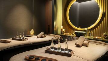 Relax in a serene spa room with two massage tables, a circular mirror, and a small table with a bowl and candles.