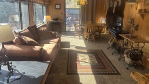 A cozy living room with a sofa, coffee table, and a dining area with chairs and a table. There is a television and decorative items on the wall.