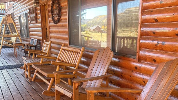 A wooden cabin with a porch featuring several Adirondack chairs and a swing set.