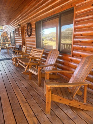 A wooden cabin with a porch featuring several Adirondack chairs and a swing set.