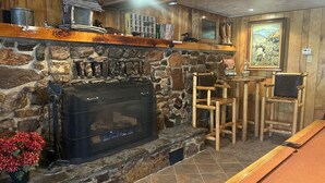 A cozy room with a stone fireplace, wooden chairs, and a pool table.