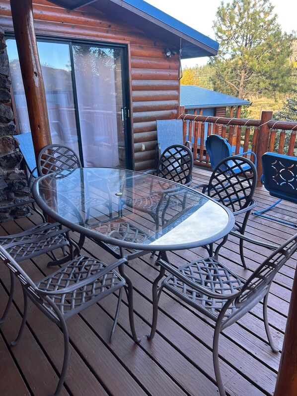 A wooden deck with a glass-top table and metal chairs.