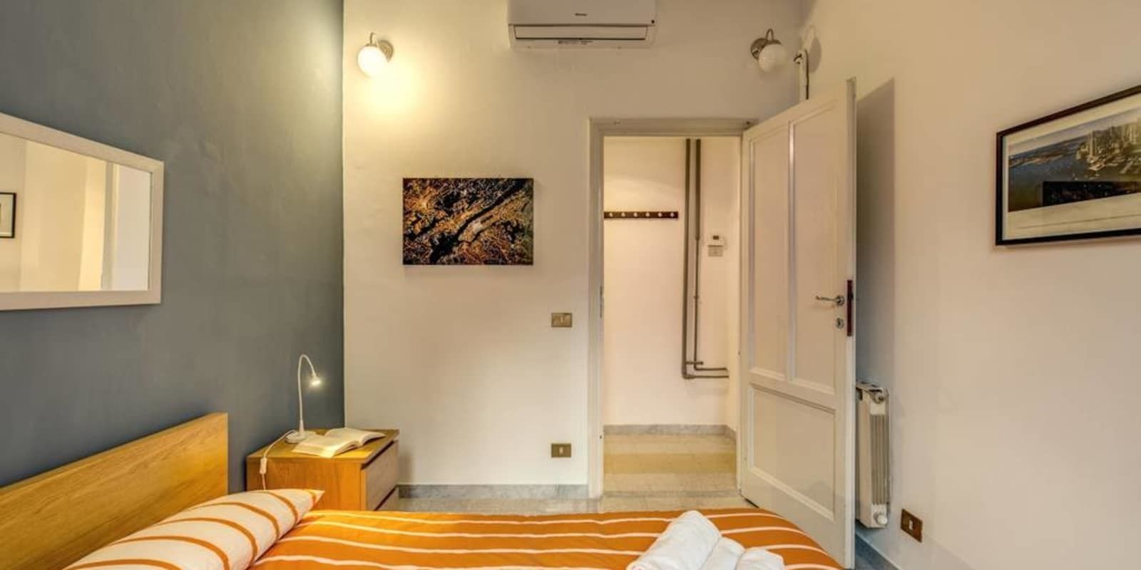A hotel room with a bed, bedside table, lamp, and artwork on the wall.