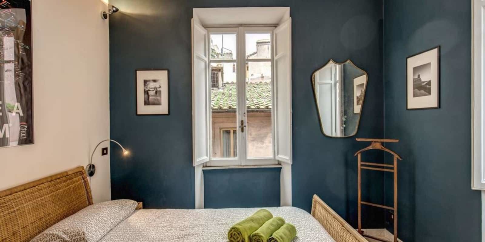 Ein Schlafzimmer mit Bett, Fenster, Spiegel und Kleiderhaken.