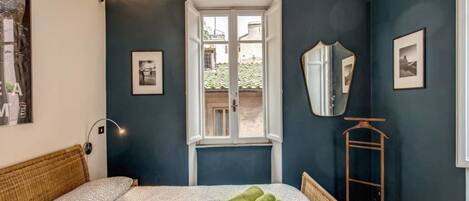 Ein Schlafzimmer mit Bett, Fenster, Spiegel und Kleiderhaken.