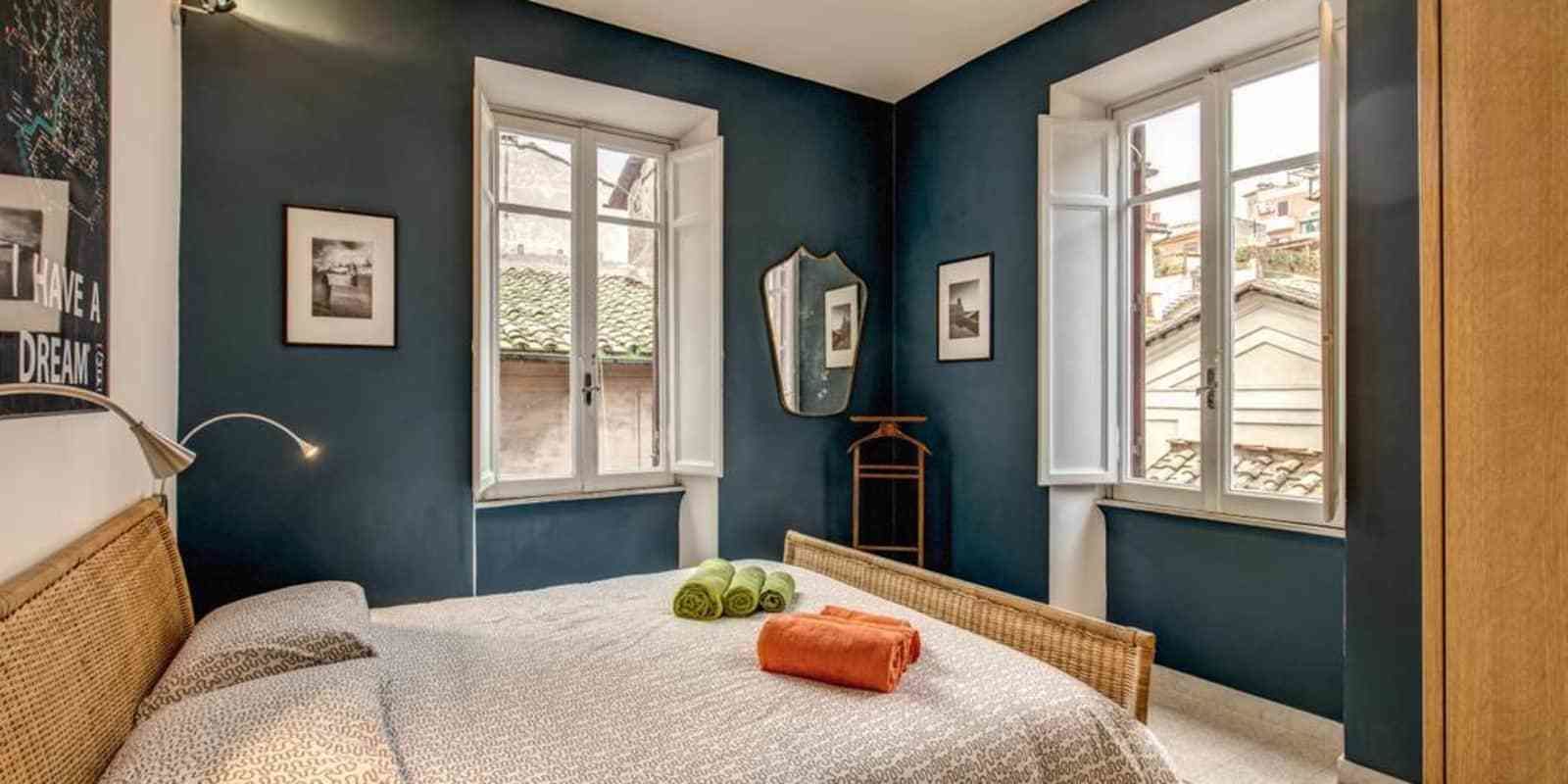 Un dormitorio con una cama, dos ventanas y un espejo.