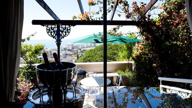 A balcony with a view of the city, a table with chairs, and a decorative metal structure. - 123 Ocean View Drive Apartment (Cape Town)