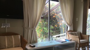 A hotel room with a bed, two wicker chairs, a glass-top table with a remote control, a book, and a decorative bowl. - 123 Ocean View Drive Apartment (Cape Town)